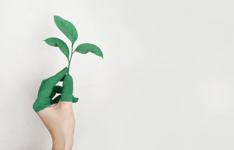 A hand covered in green paint holds a leaf between its fingers