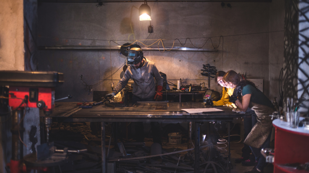 people standing around working desk, repairing metal item